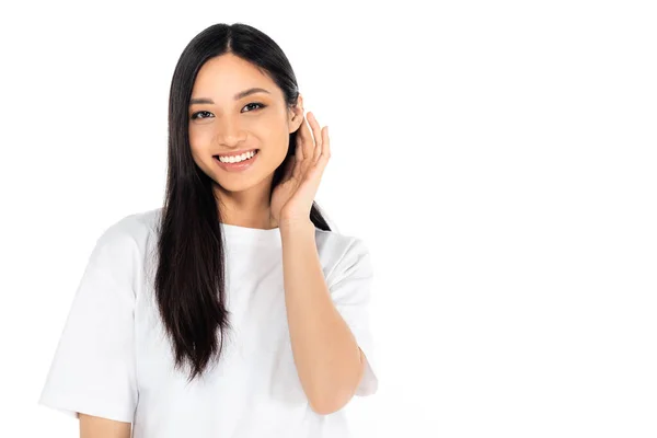 Cheerful asian woman looking at camera and fixing hair isolated on white - foto de stock