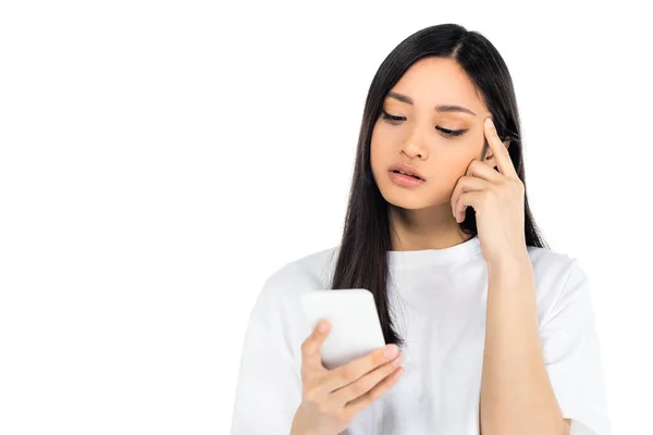 Thoughtful asian woman touching head while looking at mobile phone isolated on white — Photo de stock