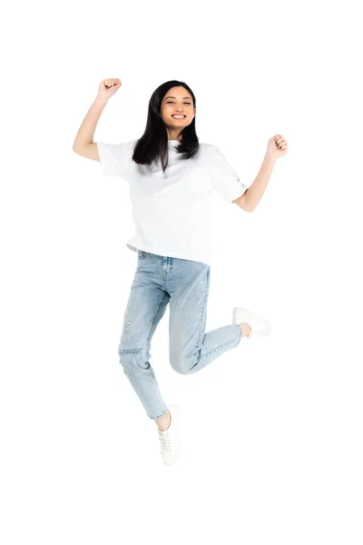 Piena lunghezza vista di allegra donna asiatica in t-shirt e jeans levitare isolato su bianco — Foto stock