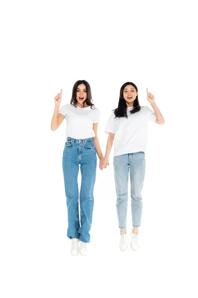 Full length view of cheerful multiethnic women pointing with fingers while levitating isolated on white - foto de stock