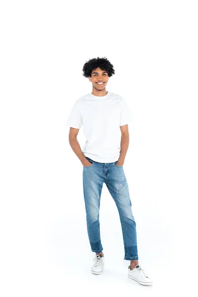 Ganzkörperansicht eines lächelnden afrikanisch-amerikanischen Mannes, der mit Händen in Jeanstaschen auf weißem Grund steht — Stockfoto