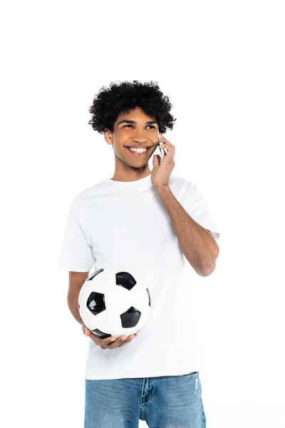 Souriant homme afro-américain avec ballon de football parlant sur téléphone mobile isolé sur blanc — Photo de stock