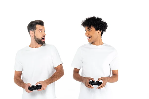 KYIV, UKRAINE - DECEMBER 5, 2021: astonished multiethnic men looking at each other while gaming isolated on white — Stock Photo