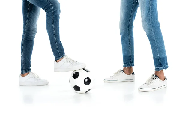 Cropped view of interracial men in jeans and sneakers playing football on white — стоковое фото