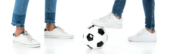 Cropped view of interracial men in jeans and sneakers near soccer ball on white, banner — Stockfoto