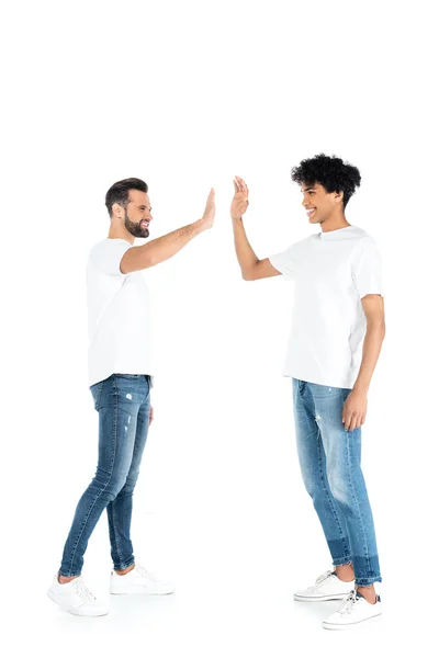 Full length view of interracial friends in jeans and t-shirts giving high five on white — Foto stock