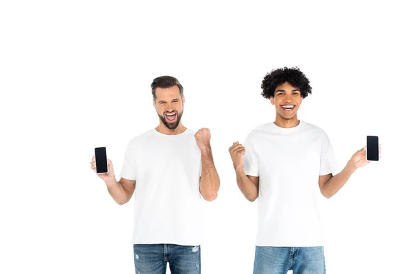 Excited interracial men with mobile phones showing yeah gesture isolated on white — Stock Photo