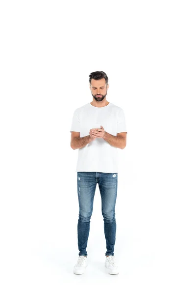 Full length view of man in jeans chatting on smartphone on white — Stock Photo