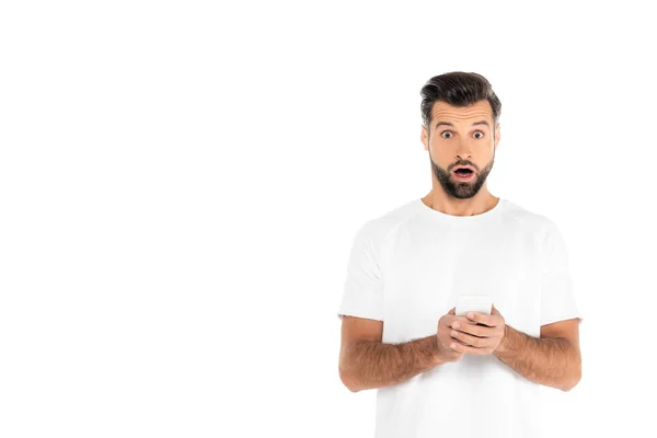 Astonished man with open mouth messaging on mobile phone while looking at camera isolated on white - foto de stock