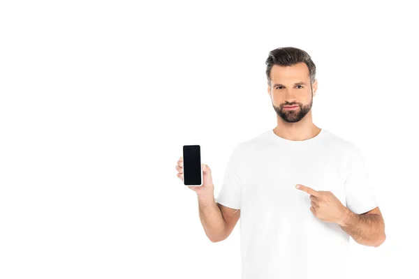 Hombre positivo mirando a la cámara y apuntando al teléfono inteligente con pantalla en blanco aislado en blanco - foto de stock