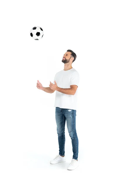 Piena vista lunghezza dell'uomo allegro in jeans che gioca con il pallone da calcio su bianco — Foto stock