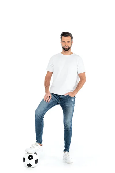 Ganzkörperansicht des Mannes, der auf den Fußball tritt, während er mit der Hand in der Hosentasche der Jeans steht, isoliert auf weißem Grund — Stockfoto