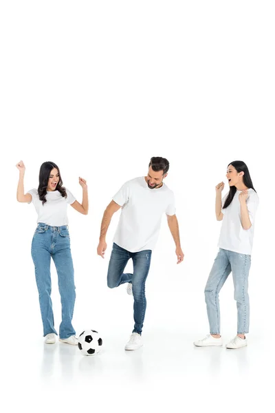 Excited interracial women showing win gesture near man playing football on white — стоковое фото