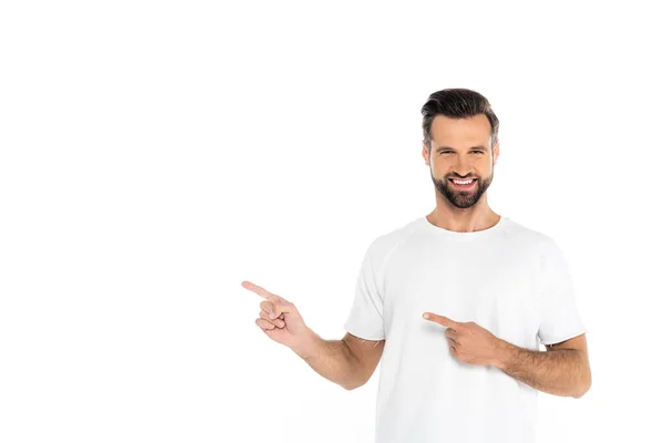 Hombre feliz en camiseta apuntando con los dedos mientras mira la cámara aislada en blanco - foto de stock