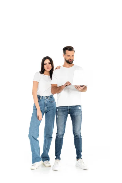 Full length view of pretty woman smiling at camera near man using laptop on white — Fotografia de Stock