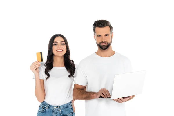 Mujer feliz celebración de la tarjeta de crédito cerca del hombre con el ordenador portátil aislado en blanco - foto de stock