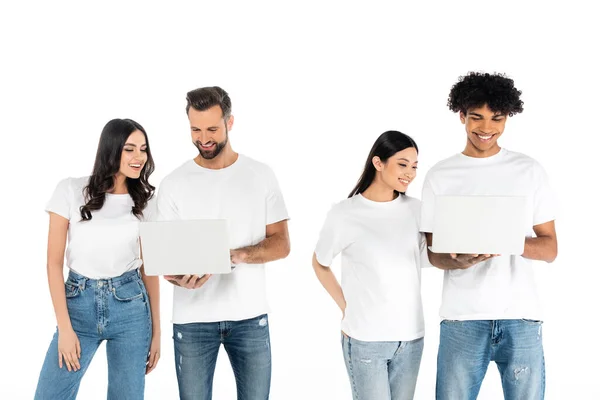 Zufriedene interrassische Männer mit Laptops in der Nähe junger Frauen isoliert auf weiß — Stockfoto