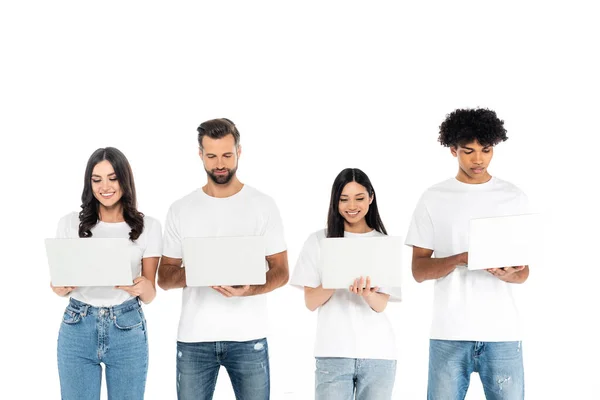 Freelancers multiétnicos sonrientes en camisetas y jeans usando computadoras portátiles aisladas en blanco - foto de stock