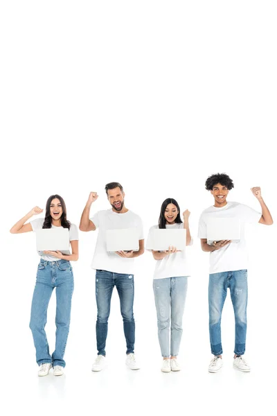 Full length view of happy multiethnic friends with laptops showing triumph gesture on white — Stockfoto