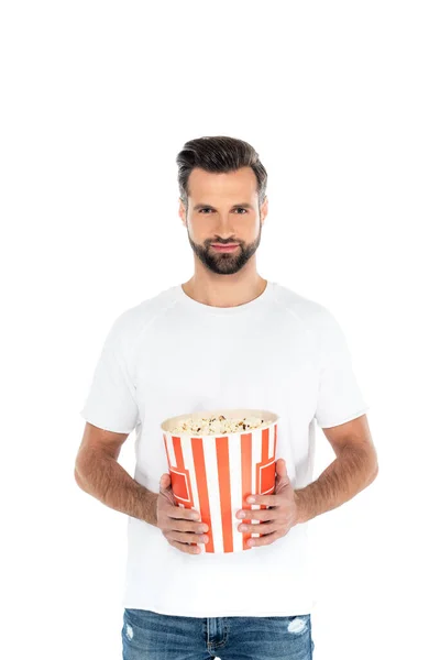Positive bearded man looking at camera while holding big bucket of popcorn isolated on white — Fotografia de Stock