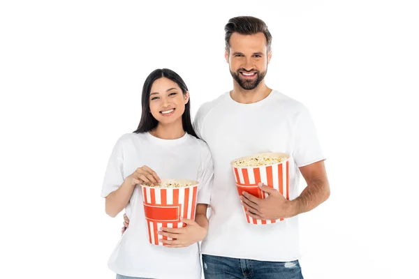 Joyful interracial couple with buckets of popcorn watching movie isolated on white — стоковое фото