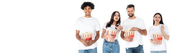 Alegres amigos multiétnicos comiendo palomitas de maíz mientras ven películas aisladas en blanco, pancarta - foto de stock