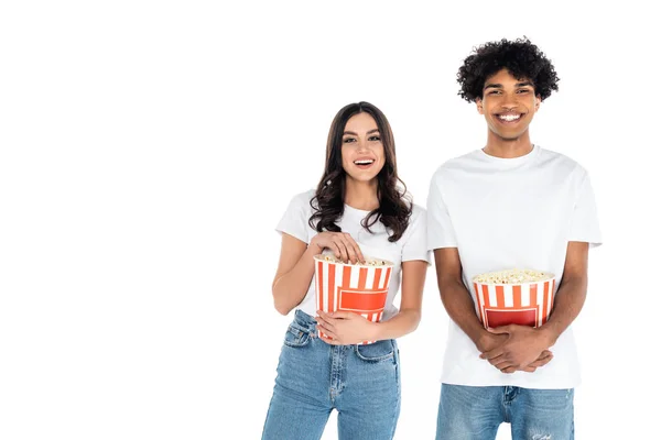 Young and happy multiethnic couple with buckets of popcorn isolated on white — Stockfoto