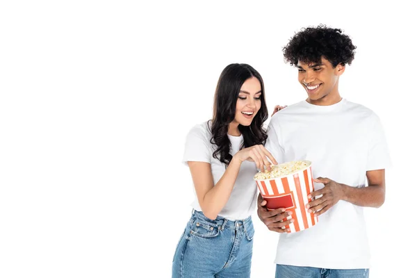 Sorridente afro-americano homem segurando pipoca balde perto mulher feliz isolado no branco — Fotografia de Stock