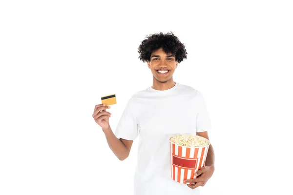 Satisfeito afro-americano homem segurando balde de pipoca e cartão de crédito isolado no branco — Fotografia de Stock