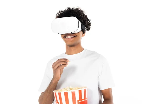 Souriant homme afro-américain manger du pop-corn tout en jouant dans un casque vr isolé sur blanc — Photo de stock