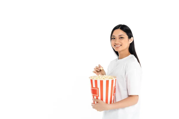 Happy asian woman in t-shirt holding big bucket of popcorn isolated on white — Stock Photo