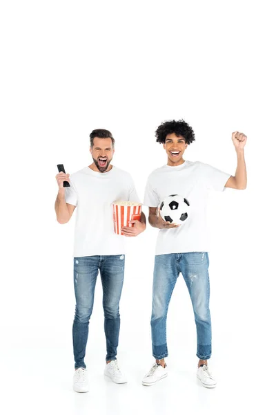 Excited interracial sport fans with soccer ball and popcorn watching football match on tv on white - foto de stock