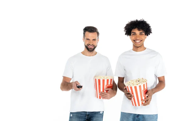 Joyful interracial men with big popcorn buckets watching tv isolated on white — Stock Photo