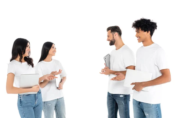 Smiling multiethnic friends with laptops pointing at each other while talking isolated on white - foto de stock