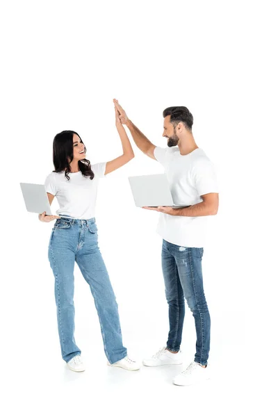 Visão comprimento total do casal satisfeito com laptops olhando um para o outro e dando alta cinco no branco — Fotografia de Stock