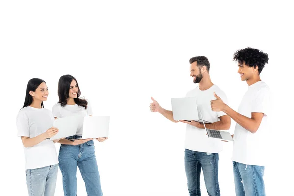 Cheerful interracial freelancers showing thumbs up to women with laptops isolated on white — Foto stock