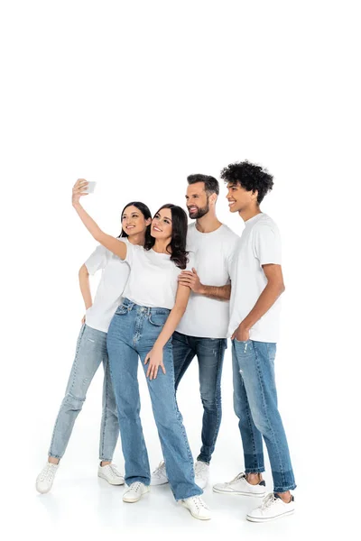 Vue pleine longueur de femme heureuse prenant selfie avec des amis multiethniques sur blanc — Photo de stock