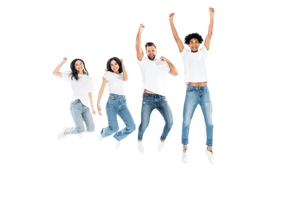 Vue complète des amis multiculturels excités en jeans montrant geste de victoire tout en lévitant isolé sur blanc — Photo de stock