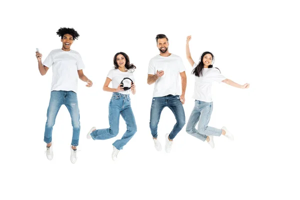 Visão completa de amigos multiétnicos com fones de ouvido e telefones celulares levitando isolado em branco — Fotografia de Stock