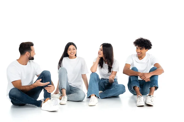 Cheerful woman pointing with hand while talking to multiethnic friends sitting on white — Stock Photo