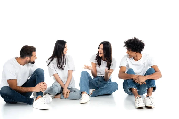 Excited woman pointing with hands while talking to smiling interracial friends sitting on white — Fotografia de Stock