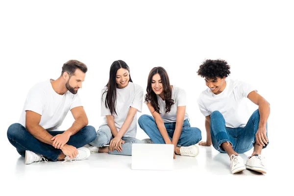 Amigos multiétnicos satisfechos viendo la película de comedia en el ordenador portátil mientras está sentado en blanco - foto de stock