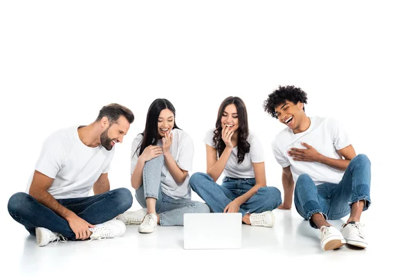 Visão de comprimento total de amigos multiétnicos rindo enquanto assiste filme de comédia no laptop no branco — Fotografia de Stock