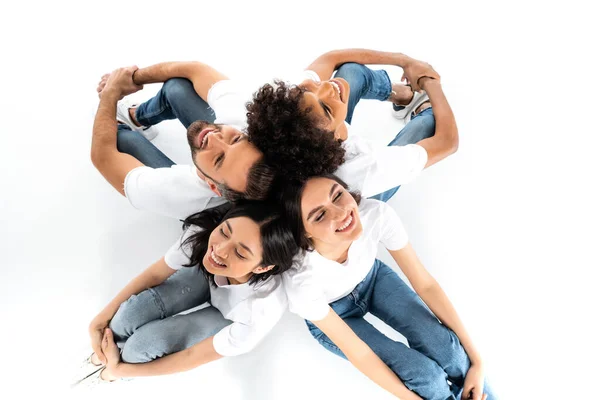 Top view of happy multiethnic friends sitting back to back on white — Fotografia de Stock