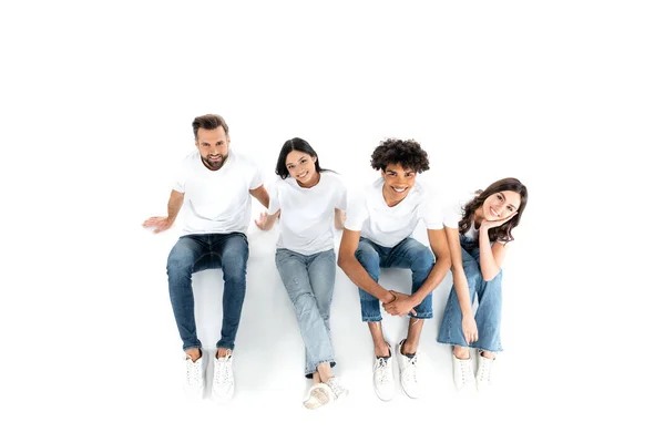 Vue de dessus des amis multiethniques heureux regardant la caméra tout en étant assis sur blanc — Photo de stock