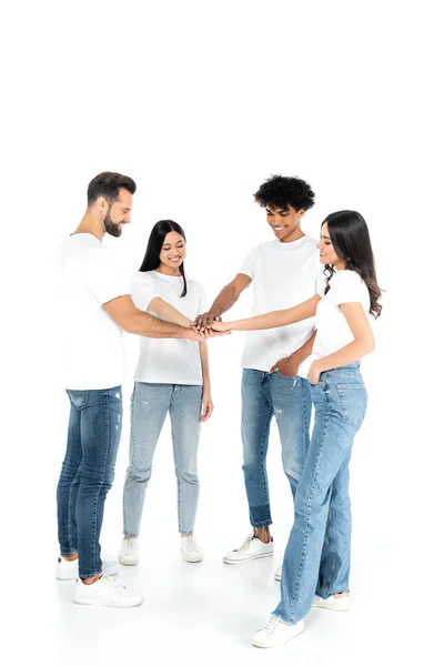 Full length view of multicultural friends in t-shirts and jeans joining hands while standing on white — Stock Photo