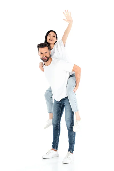 Man in jeans piggybacking excited asian woman waving hand on white — Stock Photo