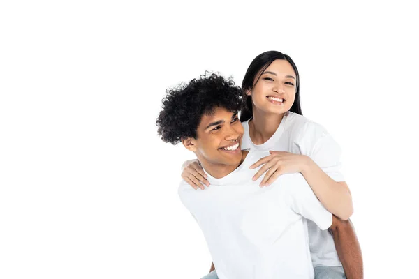 Sorridente africano americano uomo piggybacking allegro asiatico donna guardando macchina fotografica isolato su bianco — Foto stock