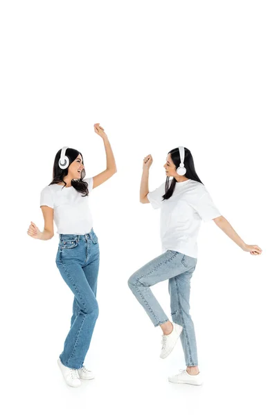 Vista completa de mujeres multiétnicas excitadas en auriculares bailando en blanco - foto de stock