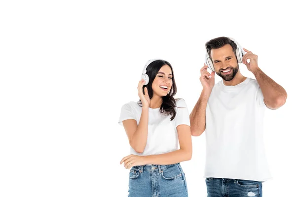 Glücklicher Mann schaut in die Kamera, während er Musik im Kopfhörer hört, mit fröhlicher Frau isoliert auf weißem Grund — Stockfoto